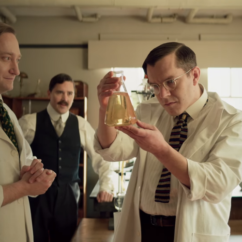 In a screenshot from the Heritage Minute on the discovery of insulin, 4 scientists in 1921 gaze at a beaker of clear liquid.