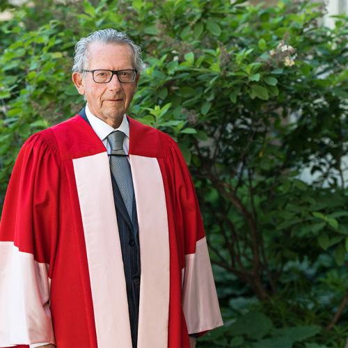 Ira Gluskin stands in a garden, wearing U of T academic robes.