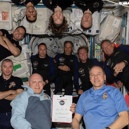 11 people pose together, floating in the air in a space station.