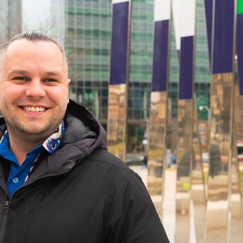 Jaris Swidrovich smiles, standing by an art installation outside the U of T Pharmacy building on College St.