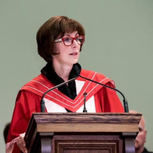 Katie Taylor, wearing academic robes, speaks at a lectern.