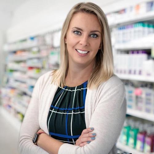 Kristen Watt smiles as she stands in front of pharmacy shelves.