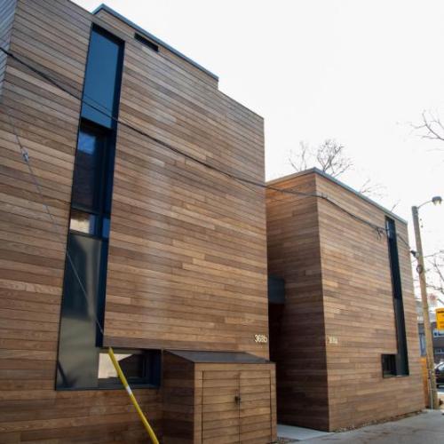 Polished wooden strips catch the sun as they line the walls of two buildings in a quiet alley.