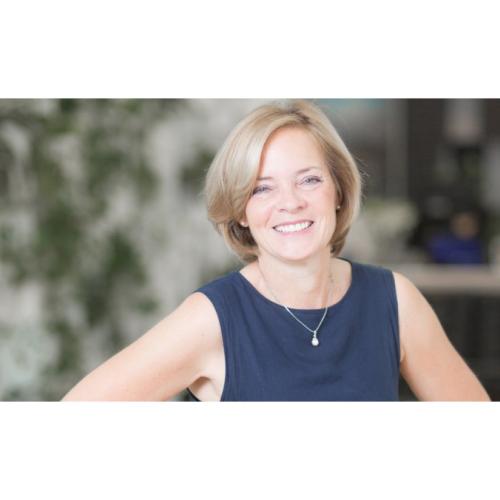 Lisa Bate smiles, hand on her hip, on a leafy city street.