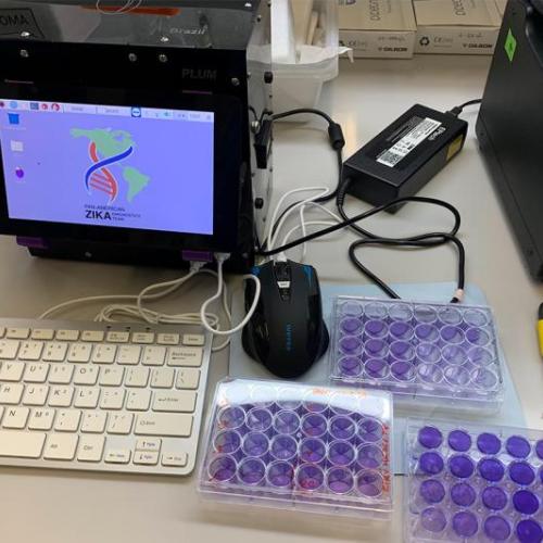 The elements of the portable rapid Zika virus test sit on a table: briefcase-sized machine, computer monitor, tray of vials.