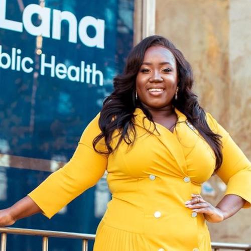 Maame De-Heer smiles happily, standing with hand on hip outside the Dalla Lana School of Public Health.