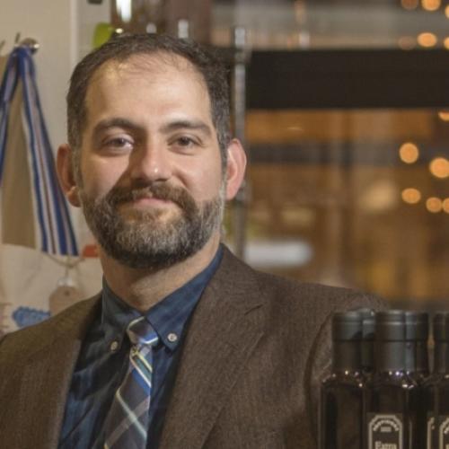 Michael Fakri smiles while sitting in an office by a desk piled with different food products.