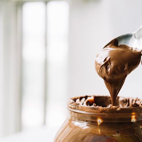 Picture of a messy jar of hazelnut chocolate spread, with a spoon lifting out a large scoop.