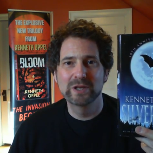 Kenneth Oppel smiles and holds up his book Silverwing in this still from a video.