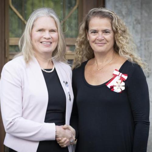 Susan Chatwood and Julie Payette smile as they shake hands. Both women are wearing medals.