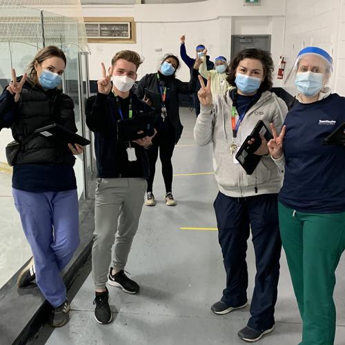 Susannah Merritt, Noah Schonewille, Upasana Saha, Cass Mackey and Erin Bearss flash victory signs at a vaccination clinic.