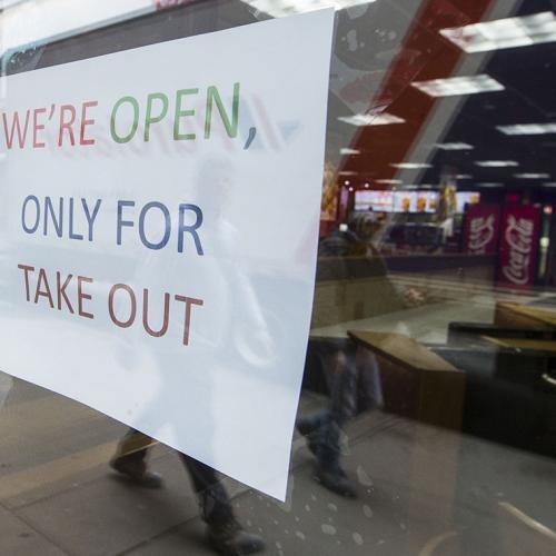 A sign in a restaurant window reads: We're open, only for take-out. 