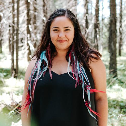 Samantha Martin-Bird smiles as she stands in a forest on a sunny day.