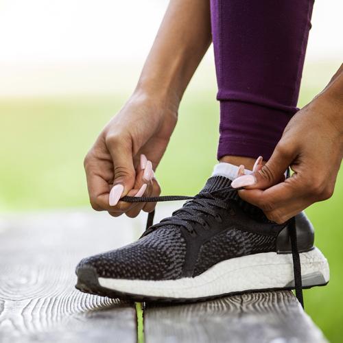 Close up on a person's hands tying a running shoe, on a bench outdoors.