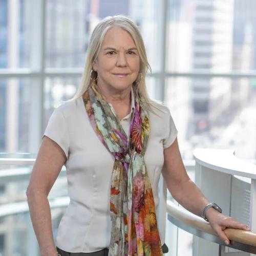 A portrait of Stinton wearing a white t-shirt with a floral scarf tied elegantly around her neck