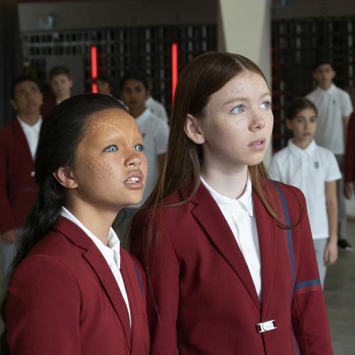 Two children wearing prosthetic makeup stand in front of several other kids wearing a school uniform.