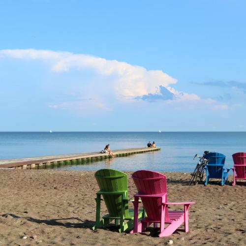 Empty Muskoka chairs sit in pairs on a sunny, deserted beach.
