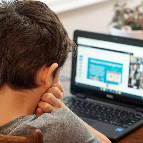 A young boy looks at a laptop screen with his head in his hands.