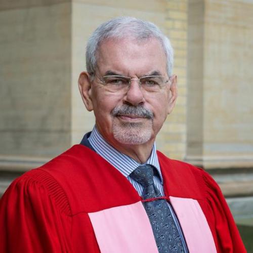 William Troost stands outside Simcoe Hall, wearing academic robes.