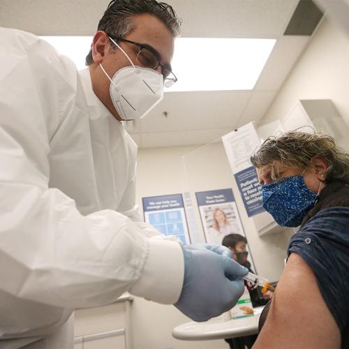A pharmacist in a mask vaccinates a masked woman in her arm.