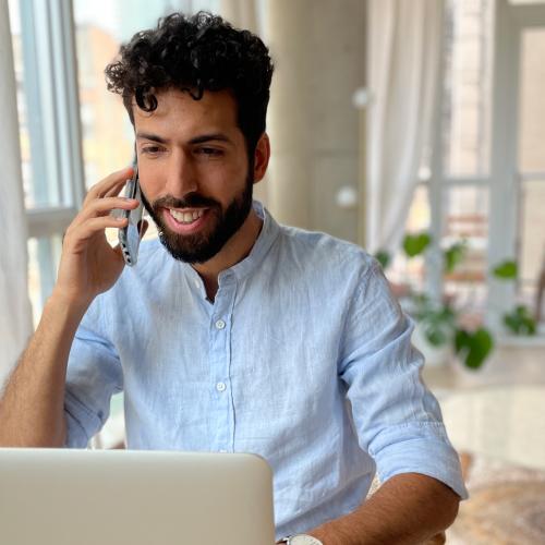 Dr. Latif Murji smiles as he sits at a laptop and talks on a smartphone.