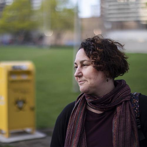 Gillian Kolla looks pensive, standing on the grass in Moss Park in front of a needle drop box.
