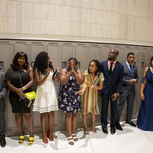 A line of well-dressed graduates smile and chat while waiting in a hallway for Black Graduation to begin.