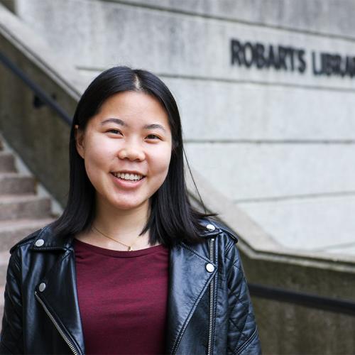 Danielle Lee smiles while standing in front of the steps to Robarts Library.