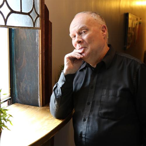 Andrew James Paterson leans on the windowsill of an old-fashioned, open window.