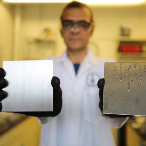 U of T researcher Tarek Awad shows two samples: a stainless steel surface treated to trap simple cooking oil (left) and an uncoated surface (photo by Liz Do) 