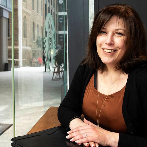 Sandra Pellegrini  smiling and sitting at a window table in a cafe, looking out on the street.