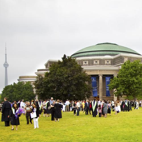 Convocation Hall in sunshine with new graduates out front on the lawn, wearing academic robes.