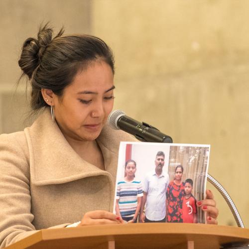 Chemi Lhamo stands at a podium, tearfully holding up a photograph of two parents with their two children. (photo by Don Campbell)