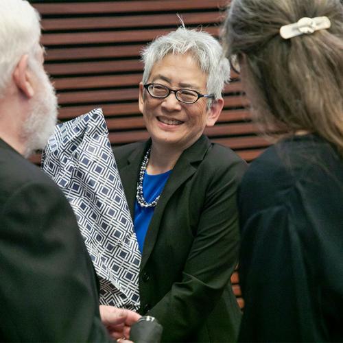 Carol Chin smiles, holding a wrapped present, as two people congratulate her.