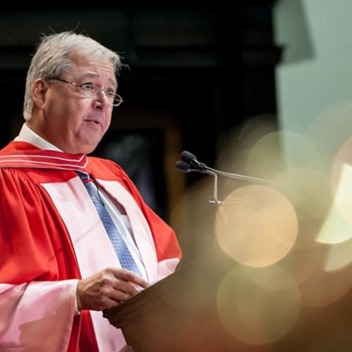 Carlo Fidani, wearing academic robes, speaks at a lectern in Convocation Hall.