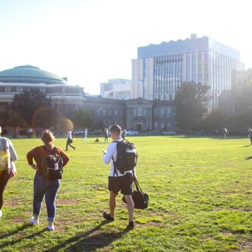 Three students walk across Front Campus. Their late afternoon shadows stretch away from Convocation Hall.