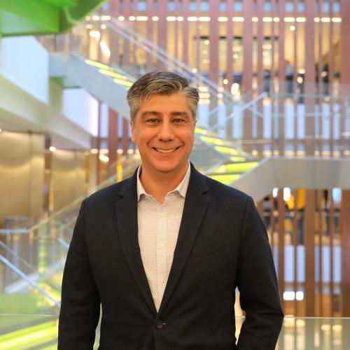 Alex Grbic smiles while standing in front of a staircase in an indoor atrium (photo by Liz Do).