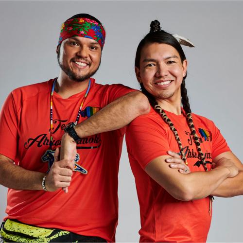 Anthony Johnson and James Makokis smiling. Makokis wears a feather and wrapped braids and Johnson wears a headband and necklace.