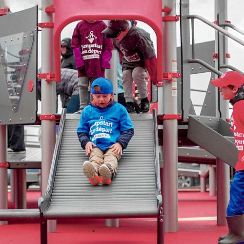 Children play on a slide made of parallel rollers, wearing T-shirts with the Jumpstart logo (photo courtesy of Canadian Tire Jumpstart Charities)