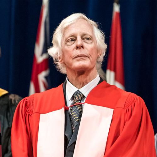 Ted Chamberlain looks serious as he stands on stage at Convocation in academic robes.
