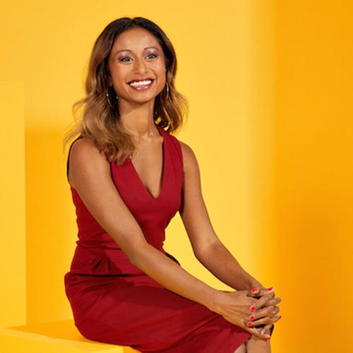 On this a page from Precedent magazine, Janani Shanmuganathan sits on a cube against a sun-coloured background, smiling.