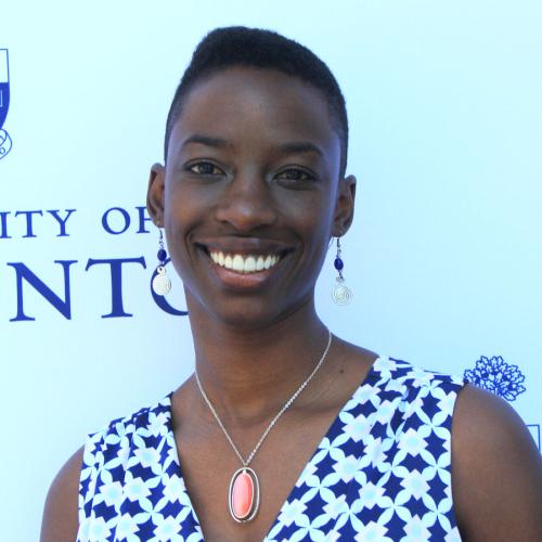 Janelle Joseph smiles while standing in front of a wall with the University of Toronto logo.