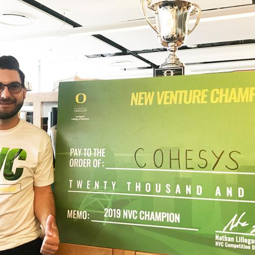 Post-doc Michael Floros smiles while posing next to a giant cheque for $20,000.