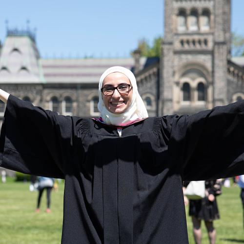 Noura AliJizawi smiles and holds out her hands as she stands on Front Campus in her graduation gown.