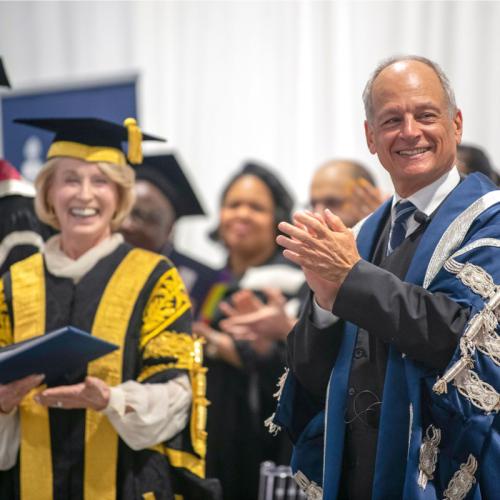 Rose Patten and Meric Gertler smile and clap, wearing academic robes.