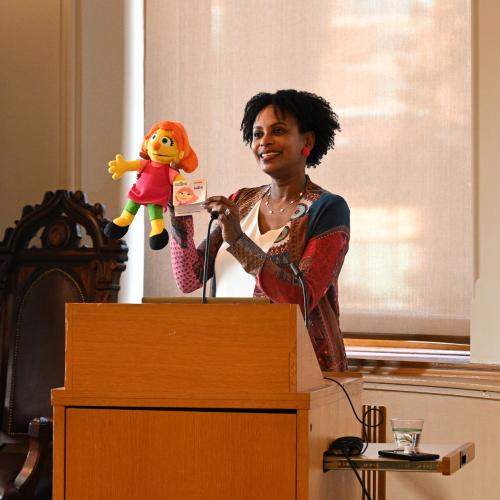Rhonda McEwen stands at a podium with her puppet Julia