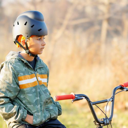 A boy stands beside his bike wearing a helmet that allows for his head covering