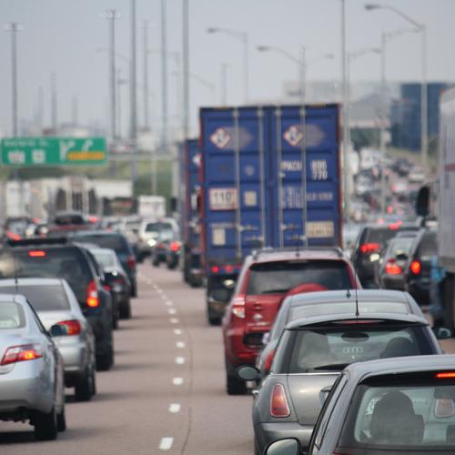 Cars sit in bumper-to-bumper traffic behind transport trucks on a highway in Toronto, before a hazy sky (photo by Danielle Scott via Flickr) 