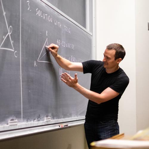 Zack Wolske gestures as he writes a geometry problem on a chalkboard.