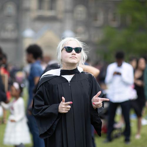 Elspeth Arbow makes finger guns as she stands on Front Campus in her academic robes and large sunglasses.